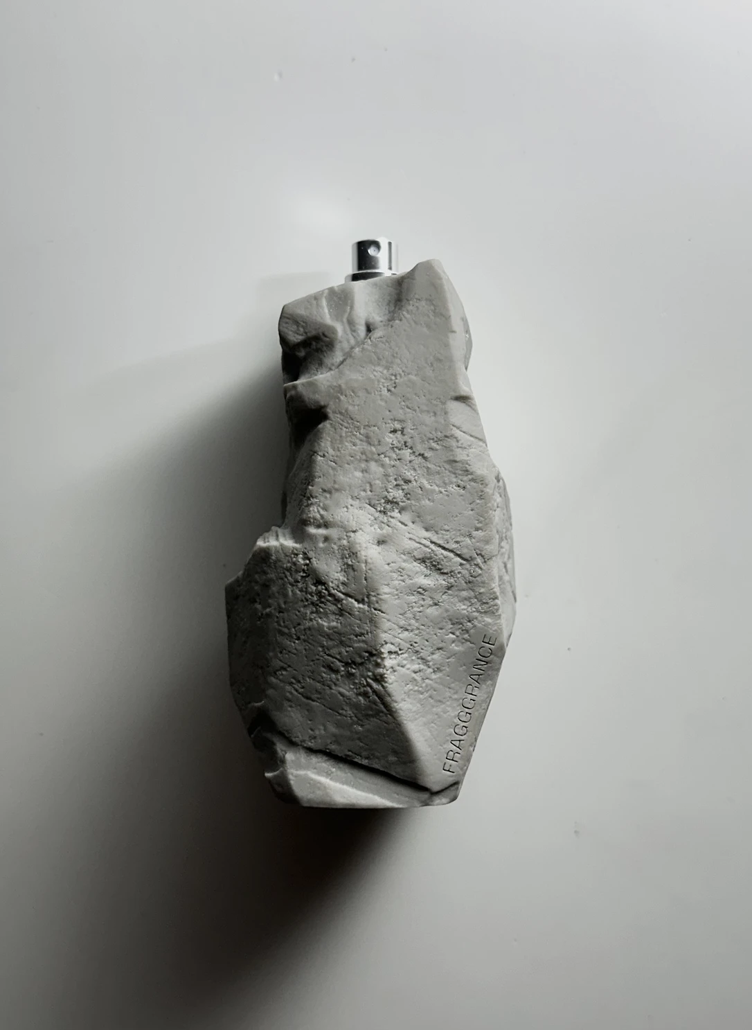 A grey 3D print of the boulder-shaped bottle with a silver spray nozzle, FRAGGGRANCE embossed on its side